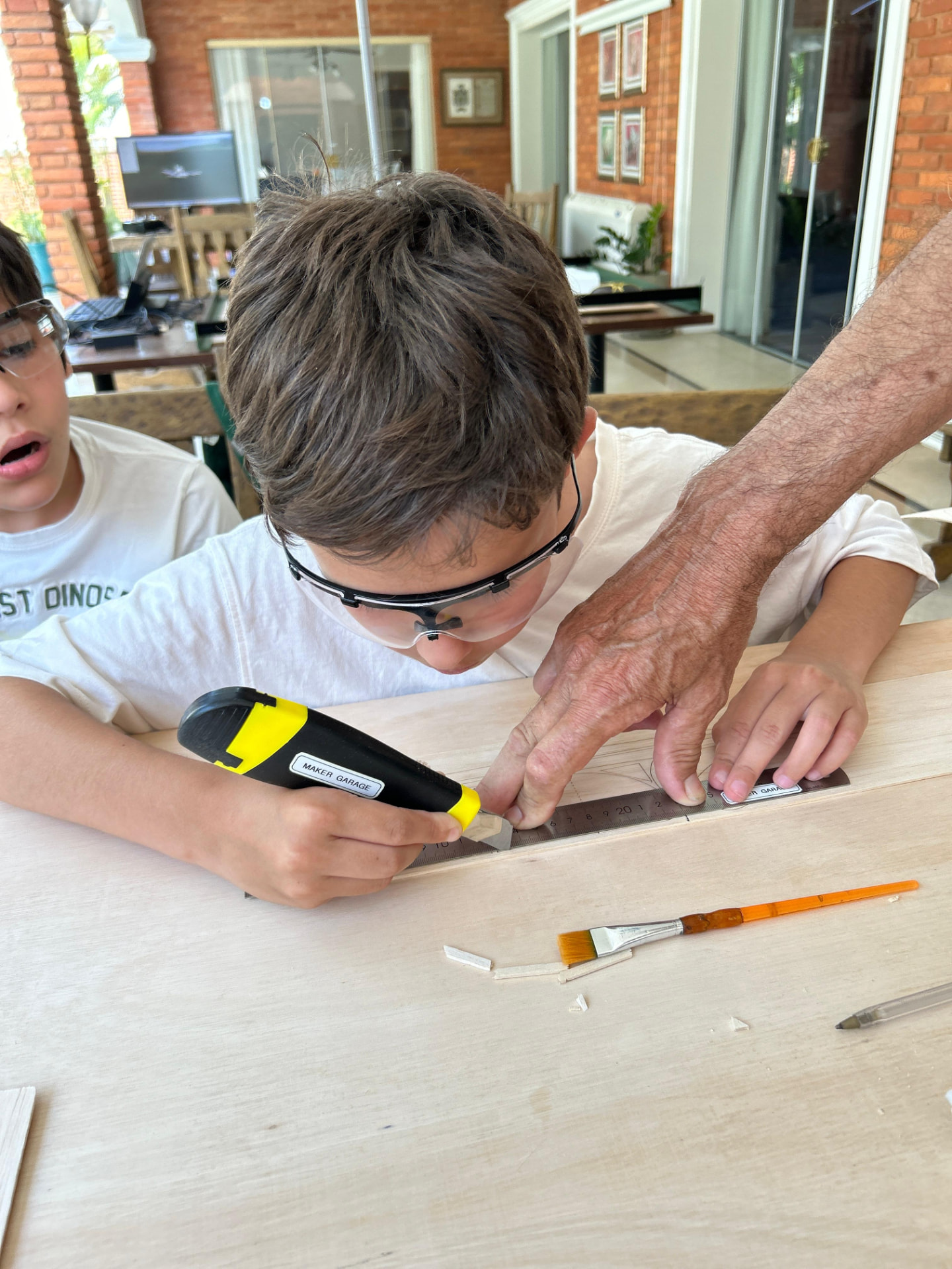 Instructor guiando a un chico que corta madera balsa con cutter y regla metálica
